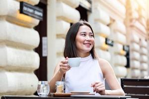 skön asiatisk ung kvinna med kopp av kaffe. kvinna åtnjuter färsk kaffe i de morgon- med soluppgång på coffe affär skön kvinna dricka kaffe i de morgon- Sammanträde utomhus foto