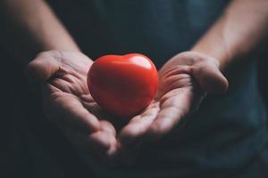 händer innehav och ger röd hjärta för kärlek, hälsa vård, organ donation, värld hjärta dag, värld hälsa dag, mindfulness, väl varelse, familj försäkring begrepp. foto