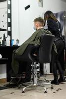 en tonåring i en skönhetssalong klipper sig, en frisör klipper en tonårspojkes hår. foto