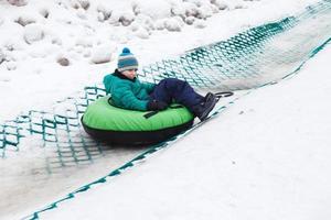barn har roligt på snö rör. pojke är ridning en slang. vinter- underhållning. unge glidning utför på rör foto