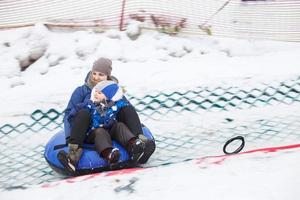 familj har roligt på snö rör. mor med unge är ridning en slang. människor glidning utför på rör foto