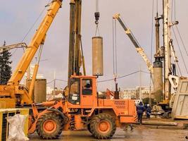 konstruktion Utrustning på de planskild reparera webbplats. stor betong block är restes förbi kranar. ett orange traktor för asfalt stenläggning enheter närliggande på stor hjul foto