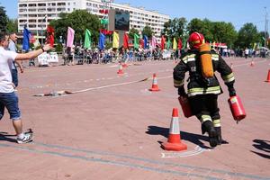 en brandman i en eldfast kostym och en hjälm löpning med röd brand släckare till släcka en brand på en brand sport konkurrens, belarus, minsk, 08.08.2018 foto