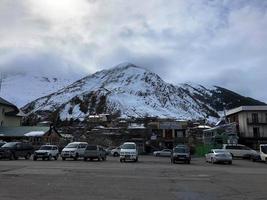 parkering och sten hus, byggnader, butiker, tankning på en skön berg vinter- tillflykt med hög berg toppar och stenar täckt med snö mot en blå himmel. georgien, tbilisi, april 17, 2019 foto