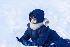 en leende Lycklig barn lögner i en snödriva på en solig vinter- dag. en massa av snö och mycket frostig. aktiva vinter- utomhus- spel. foto