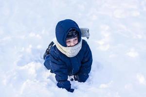 en leende Lycklig barn lögner i en snödriva på en solig vinter- dag. en massa av snö och mycket frostig. aktiva vinter- utomhus- spel. foto