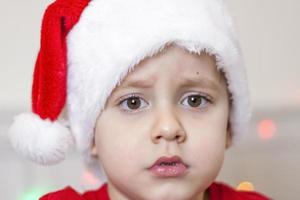 porträtt av en söt pojke i en santa claus hatt. rolig leende barn. gåvor, leksaker, glädje, firande. foto