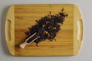 en blandning av torr svart te och torr te reste sig kronblad som en bakgrund. isolerat på en trä- yta. foto