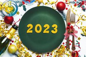 Lycklig ny år 2023. topp se av gyllene tal 2023 på tallrik för jul middag med jul prydnad och champagne flaska . ny år eve firande begrepp bakgrund foto