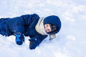 en leende Lycklig barn lögner i en snödriva på en solig vinter- dag. en massa av snö och mycket frostig. aktiva vinter- utomhus- spel. foto