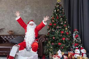 glad santa claus är omgiven förbi jul närvarande låda med fullt dekorerad chrsitmas träd för säsong firande och Lycklig ny år händelse begrepp foto