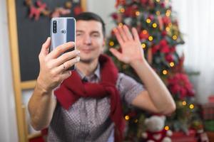 ung man nära jul träd på Hem i bekväm kläder vågor hans hand som tecken foto