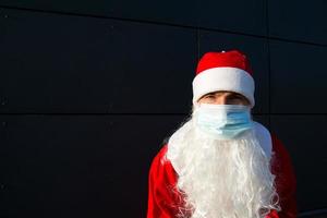 santa claus med vit skägg i röd täcka i en medicinsk mask. jul i de coronavirus pandemisk, säsong- sjukdomar, sars och lunginflammation i de högtider. skydd från virus i de ny år foto