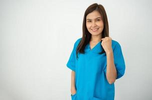 porträtt av självsäker, Lycklig, och leende asiatisk medicinsk kvinna läkare eller sjuksköterska bär blå scrubs enhetlig över isolerat vit bakgrund foto