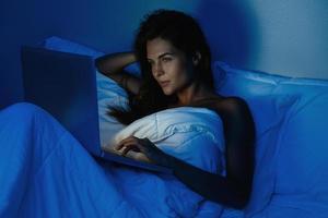 ung kvinna är använder sig av bärbar dator dator på de natt tid foto