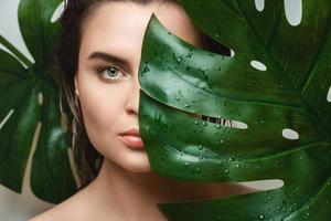 ung kvinna med en slät hud innehav monstera deliciosa växt blad foto