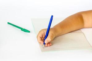de barn innehar hans händer över ett öppen anteckningsbok och är gående till skriva i Det. närbild av en barnets händer. foto