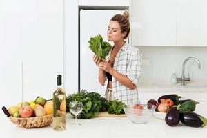 ung Söt kvinna med sniffa sallad löv under matlagning foto