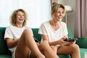 två skön flickor spelar video spel trösta i levande rum foto