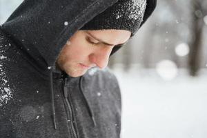 atletisk man bär luvtröja under hans vinter- träna i snöig stad parkera foto