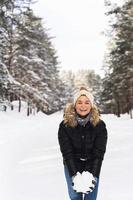 ung kvinna innehav högen av snö i henne händer under henne promenad i vinter- parkera foto