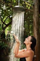 skön kvinna tar utomhus- dusch i de tropisk djungel foto