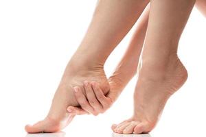kvinna försiktigt rörande mjuk hud av henne häl. kvinna fötter på vit bakgrund. foto