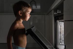 nyfiken bebis pojke öppnas de varm ugn. begrepp av säkerhet och möjlig problem med utan tillsyn barn. foto