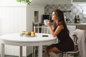 ung kvinna dricka kaffe eller te i mysigt kök foto