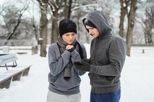 atletisk par är använder sig av smartphone under vinter- träna i snöig stad parkera foto