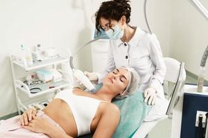 läkare och kvinna klient under radiofrekvens lyft behandling i en medicinsk estetisk klinik foto