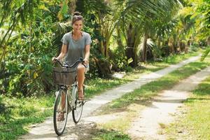 Lycklig kvinna ridning cykel i de tropisk trädgård på varm sommar dag foto