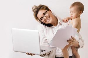 ung och upptagen affärskvinna är arbetssätt och innehav henne liten bebis foto