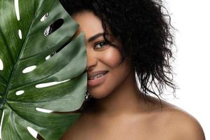 skön svart kvinna med en slät hud innehav grön tropisk blad foto