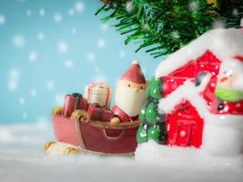 Lycklig santa claus med gåvor låda på de snö kälke gående till hus. nära hus ha snögubbe och jul träd. santa claus och hus på de snö. jul och Lycklig ny år begrepp. foto