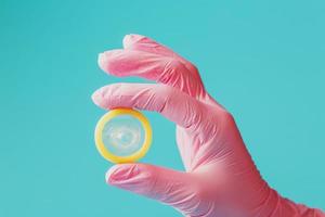 ett öppnad kondom i en hand i en rosa handske innehar på en blå bakgrund. latex för skydd mot graviditet. foto