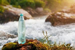 plast flaska med färsk dricka vatten på de bakgrund av en berg ström, i de vild. ool färsk vatten foto