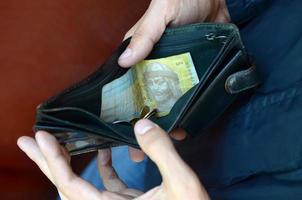 en manlig händer med mynt med små ukrainska räkningar och svart gammal handväska foto