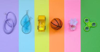 trendig modern pastell sammansättning med örhängen, solglasögon, dryck burk, basketboll boll, leksak lastbil, blomma och spinnare på bakgrund av rosa, violett, grön, orange, gul och blå färger foto