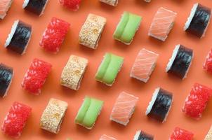 annorlunda typer av asiatisk sushi rullar på orange bakgrund. minimalism topp se platt lägga mönster med japansk mat foto