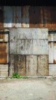 gammal byggnad täckt med rostig korrugerad tenn väggar och rullande dörr. foto