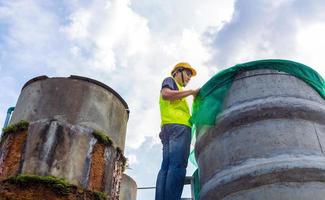 ingenjör kontrollerande de kvalitet av vatten stå på de riskabel trappa på hög platser rörelse industriell vatten rening eller filtrering Utrustning gammal cement tankar för förvaring vatten i vatten fabrik foto