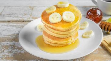 stack av banan pannkakor med skivor av färsk bananer, en ljuv hemlagad stack av pannkakor med Smör och sirap för frukost i trä- bakgrund foto