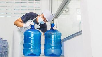 man arbetstagare i arbetskläder och med en skyddande mask på hans ansikte arbetssätt i en dryck vatten fabrik kontroll blå vatten liter innan sändning. foto