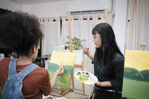 kvinna asiatisk lärare lär och demonstrerar till en studerande flicka på akryl Färg bild målning på duk i konst klassrum, kreativt inlärning med skicklighet på de elementärt skola studio utbildning. foto