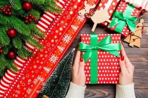 topp se av en kvinna innehav en gåva låda i henne händer på festlig trä- bakgrund. gran träd och jul dekorationer. ny år tid begrepp foto