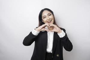 ett attraktiv ung asiatisk kvinna bär en svart kostym känner Lycklig och en romantisk former hjärta gest uttrycker anbud känslor foto
