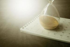 timglas på en kalender och flyter genom sandglasets glödlampa foto