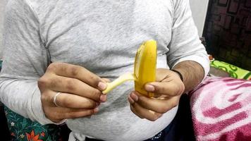 ung asiatisk man i vit t-shirt peeling banan med hand i hand foto