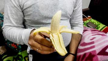 ung asiatisk man i vit t-shirt peeling banan med hand i hand foto